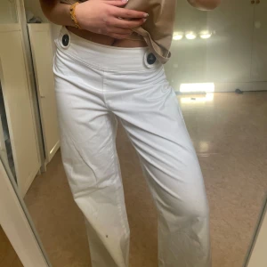 Vita vida byxor med knappar i midjan - Säljer ett par snygga vita byxor med vida ben. Byxorna stängs med dragkedja på sidan och två stora svarta knappar framtill i midjan. På mig som bär s i byxor sitter dem lite tightare i midjan, skulle säga att dem sitter mittemellan mid och higwaist. Har en liten nästintill osynlig defekt på benet, men skicket är annars bra.☺️