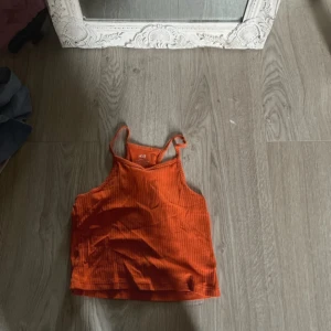 Ribbad orange linnetopp från H&M - Säljer en ribbad orange linnetopp från H&M i ekologisk bomull. Toppen har smala axelband och är perfekt för varma dagar. Enkel och stilren design som passar till mycket.