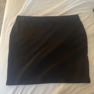 Svart kortkjol - En enkel och stilren svart kortkjol med rak passform. Perfekt att matcha med olika toppar för en trendig look. Kjolen har inga synliga detaljer eller mönster och är lätt att styla.