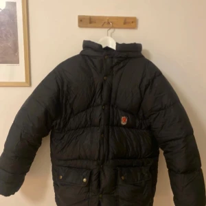 Svart dunjacka från Fjällräven - Varm och tjock svart dunjacka från fjällräven. Har två defekter som visas på två sista bilderna, men är inget man tänker på eller ser lätt. Stor i storleken.