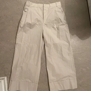 Beige vida kostymbyxor från Zara - Säljer ett par beige kostymbyxor från Zara med vida ben och hög midja. Byxorna har pressveck framtill, diskreta fickor och stängs med dragkedja och knapp. Perfekta för en stilren och trendig look.