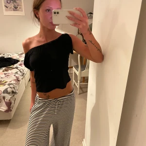 Svart oneshoulder croppad topp - Säljer en svart croppad topp med oneshoulder-design. Toppen har en dekorativ kant längs halsringningen och sitter tight. Perfekt för dig som vill ha en trendig och stilren look.