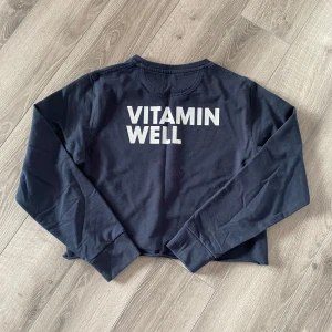 Mörkblå croppad tröja från Vitamin Well - Mörkblå croppad långärmad tröja med trycket 'VITAMIN WELL' i vitt på ryggen. Tröjan har en enkel och stilren design, perfekt för en avslappnad look. Tillverkad i mjukt bomullsmaterial.