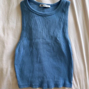 Blå ribbad tanktop från Zara - Säljer en blå ribbad linnetopp från Zara. Toppen är ärmlös med rund halsringning och croppad passform. Perfekt för varma dagar eller som ett lager under en skjorta.