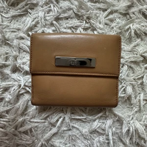 Vintage Gucci plånbok- autentisk från 2005  - Tjena! Min mor bad mig sälja denna plånboken köpt i 2005 från Gucci i Kifissia, Aten. Plånboken är gjort av ett starkt och hållbart läder i dess naturliga bruna färg. Den har en liten clip för exkta säkerhet och en liten ”metalplåt” med Guccis logga på utsidan. Plånboken är knappt använd och som ny, både på insidan och utsidan. Den enda defekten är ett litet skrap på ”clipet” däremot inget som syns eller känns.  Perfekt för både män och kvinnor. Hör av er vid minsta intresse! 
