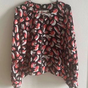 Mönstrad bomberjacka från 365 - Säljer en färgglad bomberjacka / blus / topp från 365 med svart bas och abstrakt mönster i rött, vitt och beige. Jackan har dragkedja framtill, långa ärmar och resår vid ärmslut och nederkant. Använd ett fåtal gånger