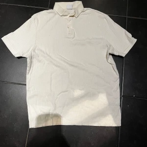 Vit ribbad piké från Zara - Säljer en stilren vit pikétröja från Zara med ribbad struktur och klassisk krage. Tröjan har korta ärmar och knäppning med tre knappar framtill. Perfekt för en clean och fräsch look samt perfekt för sommaren. 