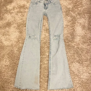 Ljusblå bootcut jeans från Nelly - Ljusblå jeans med bootcut passform från Nelly. Byxorna har slitna detaljer vid knäna och råa kanter nertill. Klassisk femficksmodell med broderade bakfickor och hög midja. Perfekta för en avslappnad och trendig look. Lite slitna längst ner eftersom de är avklippta. Midjemått:33cm innerbenslängd:80cm