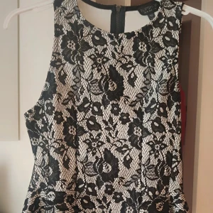Svartvit top från Topshop - Säljer en svartvit top från Topshop med vackert blommigt spetsmönster. Topen är ärmlös, har rund halsringning och dragkedja i ryggen. Tillverkad i 100% polyester och passar perfekt för festliga tillfällen.