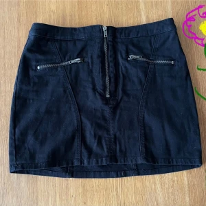 Minikjol med dragkedjor  - Svart Minikjol med dragkedjor. Två fickor fram. HM Divided, st. 40. Som M ej L Längd 36-37 cm. Linning 2 x 38 cm. Mycket fint skick, aldrig använd - som ny. Typ svart jeanstyg med elasta. #lena6800kjolar