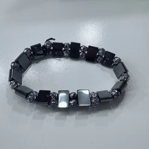 Svart armband med rosdetaljer - Säljer ett coolt svart armband med fyrkantiga pärlor i metall-look och små silverfärgade rosor mellan varje pärla. Armbandet är elastiskt och passar de flesta handleder. Perfekt accessoar för att lyfta din stil!