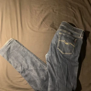 Blå jeansbyxor från Replay - Säljer ett par klassiska blå jeans från Replay med snygga kontrastsömmar och broderad bakficka. Jeansen har normal passform och är perfekta för dig som gillar stilrena och tidlösa plagg.