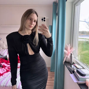 Svart långärmad klänning med rosettdetalj Magda Butrym H&M - Säljer en svart, figurnära klänning med lång ärm och snygg rynkning längs midjan. Klänningen har en stor dekorativ rosett framtill vid halsen och en liten öppning under. Perfekt för dig som vill sticka ut med en elegant och unik look.