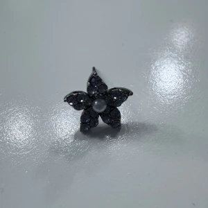 Blomformad örhänge med svarta stenar och pärla - !!!!!DET FINNS BARA EN!!!!!!!    Säljer ett örhänge i form av en blomma med svarta glittriga stenar och en vit pärla i mitten. Perfekt accessoar för att lyfta din stil med en unik detalj.