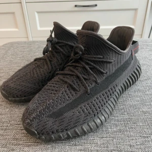 Adidas Yeezy Boost 350 V2 'Black' - Säljer ett par Adidas Yeezy Boost 350 V2 i helsvart färg. Skorna har stickad ovandel, snörning och en tydlig rand längs sidan. Sulan är ribbad och ger en sportig look. Perfekta för dig som gillar streetwear och vill ha något unikt på fötterna.