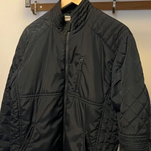 Svart quiltad jacka från Murrey - Snygg svart jacka från Murrey med quiltade detaljer på ärmar och sidor. Jackan har dragkedja framtill, ståkrage och flera fickor med dragkedja. Perfekt för dig som vill ha en stilren och sportig look.