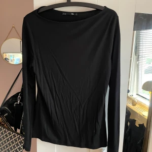 Svart långärmad topp från 157 - En enkel och stilren svart tight långärmad topp från 157. Modellen har rund halsringning (boat neck) och är tillverkad i ett mjukt material som passar perfekt till många olika outfits. Tröjan är använd 1-2 gånger. 