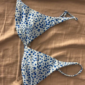 Blåvit bikiniöverdel med prickigt mönster - Snygg bikiniöverdel i trekantsmodell med blå prickar på vit botten. Justerbara band i nacken och runt ryggen för perfekt passform. Perfekt för strand eller poolhäng!