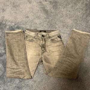 Grå jeansbyxor från Replay modell thad  - Säljer ett par grå jeansbyxor från Replay med klassisk femficksdesign och raka ben. Byxorna har knappgylf och tydliga sömmar på bakfickorna. Perfekta för dig som gillar en stilren och enkel look.
