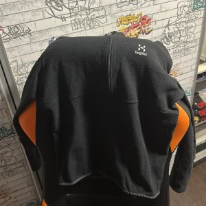 Svart fleecejacka från Haglöfs - Säljer en svart fleecejacka från Haglöfs med halv dragkedja framtill och broderad logga på bröstet. Perfekt för lager-på-lager och outdoor. Mjuk och skön mot huden.