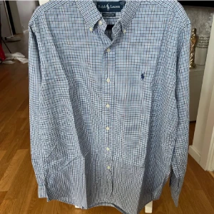 Blårutig skjorta från Ralph Lauren - Klassisk blårutig skjorta från Ralph Lauren i bomull. Skjortan har lång ärm, knappar framtill och button-down krage. Perfekt för en stilren och tidlös look. Broderad logga på bröstet.