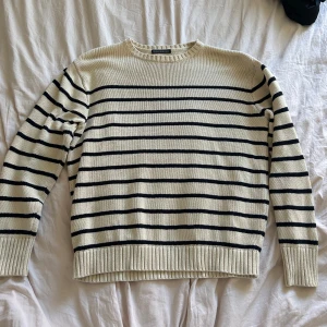 Randig stickad tröja från Brandy Melville - Säljer en beige stickad tröja med svarta horisontella ränder. Tröjan har rund halsringning, långa ärmar och ribbade muddar vid ärmslut och nederkant. Perfekt för lager-på-lager och enkel att matcha. Liten fläck vid mudden nere (se bild 3)