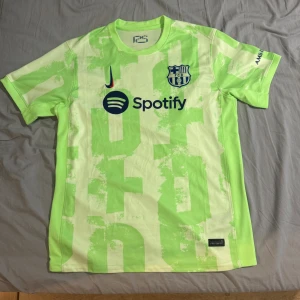 FC Barcelona tredjetröja 2024/25 - Säljer en FC Barcelona tredjetröja från säsongen 2024/25 i ljusgrönt med neongröna detaljer. Tröjan har klubbmärke , Spotify-logga och UNHCR-tryck. Kortärmad modell i lätt och ventilerande material, perfekt för match eller träning.