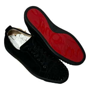 Svarta sneakers med nitar från Christian Louboutin - Säljer ett par svarta sneakers från Christian Louboutin med klassisk röd sula och svarta nitar på tån. Skorna har snörning och är tillverkade i mocka med en platt sula. Perfekt för dig som vill sticka ut med en lyxig och edgy stil.