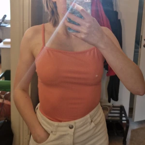 Ribbad persikofärgad bodysuit från NA-KD - Säljer en ribbad bodysuit i persikofärg från NA-KD i strl XS. Den har smala axelband, croppad passform och snygg snörning i ryggen. Materialet är mycket stretchigt, den sitter dock lite för tight för min smak. Endast använd fåtal gånger. Skriv vid frågor!✨️ Samfraktar gärna så kika in mina andra inlägg!✨️