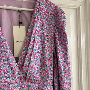 Adoore Amalfi klänning - Superfin, helt ny,  kort blommig klänning från Adoore med v-ringning och puffärmar. Klänningen har rosa, lila och blått blommönster, markerad midja och lätt rynkade detaljer längs sidorna. Sitter så fint på kroppen. Perfekt för vår och sommar men är tyvärr för liten för mig, därav att den aldrig använts! Denna är helt slutsåld på adoores hemsida. Kom med bud!💘