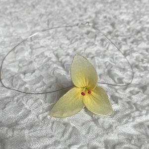 Halsband  - Unikt handgjort halsband med en stor, ljusgul blomma i tyg och små rosa pärlor i mitten. Blomman har tre kronblad och sitter på en tunn, silverfärgad metalltråd. Perfekt för dig som vill sticka ut med en söt accessoar.✨🫶