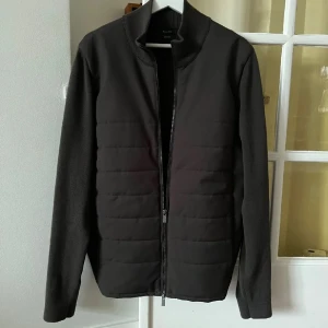 Svart quiltad jacka med dragkedja - Snygg svart jacka med quiltad front och släta ärmar. Jackan har en hög krage och hel dragkedja framtill. Perfekt för dig som gillar en stilren look med sportig touch.