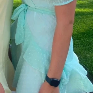 Ljusblå kortklänning med volanger - Superfin ljusblå kortklänning med volanger och knyt i midjan. Klänningen har korta ärmar och ett diskret prickigt mönster i tyget. Perfekt för sommarens alla tillfällen!