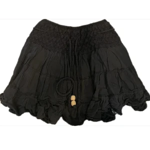 Svart volangkjol från Mizumi - Supersöt svart kortkjol från Mizumi med volanger, smockad midja och knytband med träpärlor. Står storlek M/L men skulle säga att den passar xs/S. 