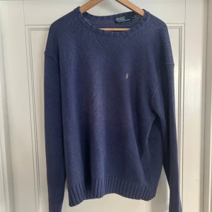 Blå stickad tröja från Polo Ralph Lauren vintage från 90 tal - Säljer en klassisk blå stickad tröja från Polo Ralph Lauren. Tröjan har rund halsringning, ribbade muddar och en liten broderad logga på bröstet. Perfekt för lager-på-lager och enkel att matcha med jeans eller chinos. Även denna tröja är inköpt på 90 talet vilket gör värdet högre. Knappt använd! Vilken deal. Materielet är 100 procent bomull och kommer räcka dig en livstid!