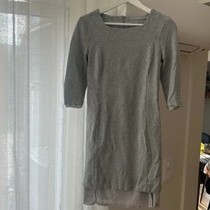 Grå klänning med trekvartsärm från tiger of Sweden - Snygg grå klänning från Tiger of Sweden med trekvartsärmar och rund halsringning. Klänningen har en rak passform och är tillverkad i mjukt bomullsmaterial. Perfekt för dig som gillar enkel och stilren design. Inneklänningen är trasig och behöver sy fast men annars så fin på