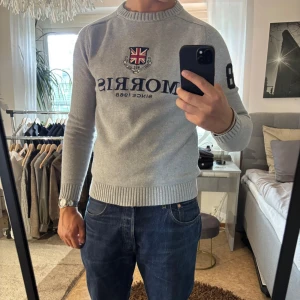 Grå stickad tröja från Morris - Snygg grå stickad tröja från Morris med broderad Union Jack-logga och text på bröstet. NYSKICK!!🌟 Storlek S. Tröjan har ribbade muddar, rund hals och svart siffra 8 på ena ärmen. 