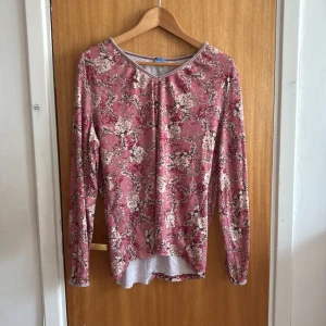 Blommig långärmad topp från Halens - Supersöt långärmad topp i rosa med blommigt mönster från Casual by Halens. Tunt och mjukt material, lätt v-ringad hals och något längre baktill. Perfekt för dig som gillar romantiska vibes och vill ha en bekväm men snygg look.💗 Dock har den en del defekter som visas på bilderna.🫶