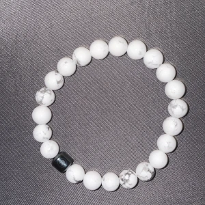 Vitt pärlarmband med marmormönster - Stilrent armband med runda vita pärlor och diskret grått marmormönster. En svart fyrkantig pärla ger en cool kontrast. Perfekt accessoar för att lyfta din outfit med en minimalistisk touch.