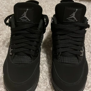 Svarta Air Jordan 4 Retro sneakers - Snygga helsvarta Air Jordan 4 Retro sneakers size 39 med klassisk Jumpman-logga på plösen och hälen. Skorna har meshpaneler, robust snörning och detaljer i syntet och skinn. Perfekta för dig som gillar streetstyle och vill sticka ut med en ikonisk siluett. Säljer skorna för dom var för små för mig. Har använt en gång