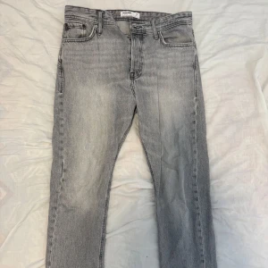 Grå jeans från Jack & Jones - Snygga grå jeans från Jack & Jones med klassisk femficksdesign och coola bakfickor med broderad detalj. Jeansen har en rak passform och är tillverkade i mjukt bomullstyg. Perfekta för dig som gillar en avslappnad men stilren look.
