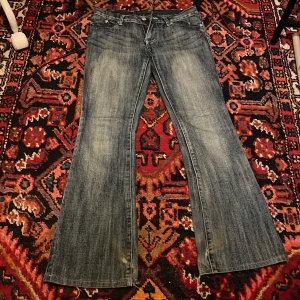 Victoria Beckham bootcut jeans med brodyr - Midjemått: 36/37cm innerbenslängd:78cm.Snygga bootcut jeans från Victoria Beckham i tvättad blå denim. Bakfickorna har broderade kronor som ger en lyxig vibe. Klassisk femficksmodell med låg midja och slitna detaljer vid benslut. Perfekta för dig som gillar statement-jeans. Gylfen har även gått sönder men de e inget man tänker på så mycket men de kan man lätt fixa hemma om man har rätt verktyg eller hos en skräddare🫶🏼