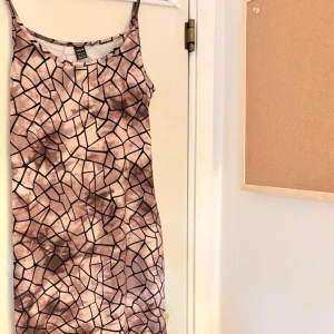 Beige mönstrad kortklänning från SHEIN - Snygg kortklänning från SHEIN med unikt grafiskt mönster i beige, svart och bruna toner. Klänningen har smala axelband och figurnära passform. Materialet är mjukt och stretchigt. Storlek: 38
