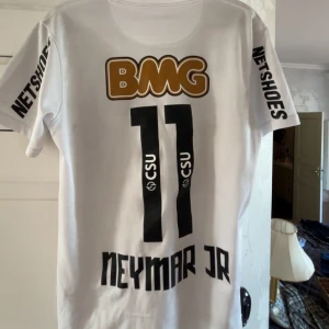 Vit Santos Neymar Jr fotbollströja Nike - Santos FC fotbollströja med Neymar Jr och nummer 11 på ryggen. Vit med svarta tryck, BMG och Netshoes-loggor samt klubbmärke på bröstet. Kortärmad modell i lätt och ventilerande Dri-FIT-material, perfekt för match eller träning.