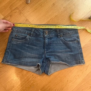 Blå lågmidjade jeansshorts från Only - Snygga blå lågmidjade jeansshorts från Only med klassisk femficksdesign och normal passform. Shortsen har midwaist, bälteshällor och knapp- samt dragkedjestängning. Perfekta för sommardagar och enkla att matcha med allt.