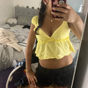 Gul croppad blus med volang - Superfin gul blus med omlott och v-ringning. Toppen är croppad och har volang nertill samt korta puffärmar. Perfekt för sommardagar och ger en fräsch look till din outfit.