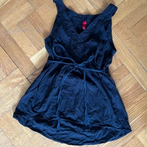 Svart linnetopp från Vero Moda - Svart linnetopp från Vero Moda med v-ringning och volangdetaljer längs halsringningen. Toppen har knytband i midjan som kan knytas både där fram och bak🩷🩷