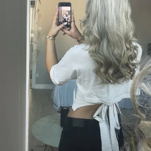 Vit croppad topp med knyt i ryggen - Säljer en vit croppad topp med kort ärm och snygg knytning i ryggen. Toppen har ett litet hål i bak vid knutet, syns inte jättemycket och borde va enkelt att laga