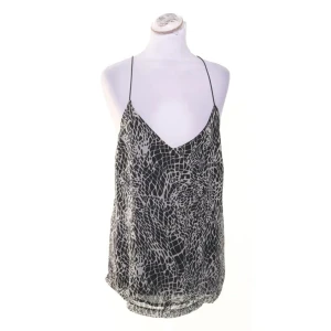 Svartvit mönstrad topp med tunna band - Säljer en svartvit linnetopp med unikt grafiskt mönster och tunna axelband som korsas i ryggen. Toppen har djup v-ringning och är tillverkad i ett lätt, luftigt material som känns skönt mot huden. Perfekt för dig som gillar en stilren men edgy look. Storlek saknas men gissar på M