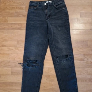 Svarta ripped jeans från Perfect Jeans - Säljer ett par svarta jeans från Perfect Jeans med snygga slitningar och hål på båda knäna. Modellen har fem fickor, dragkedja och knapp framtill samt klassisk passform. Jeansen är i ett mjukt denimtyg och har en cool, mörk tvätt.